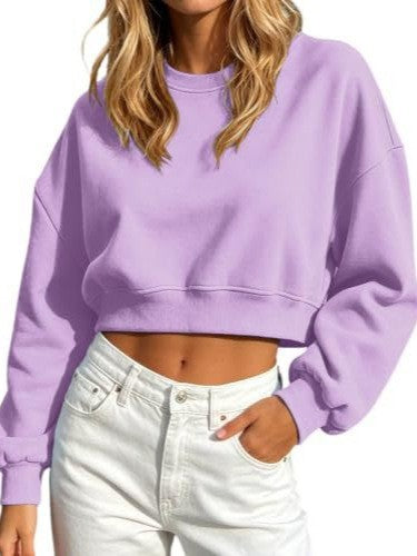 A woman wearing a lavender purple cropped crewneck sweatshirt and white jeans, shown from the neck down against a plain white background.