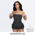 A woman modeling a dark gray strapless denim romper with a button-front bodice and shorts, shown against a light gray studio background with the brand name Aura Attire visible in the lower right.