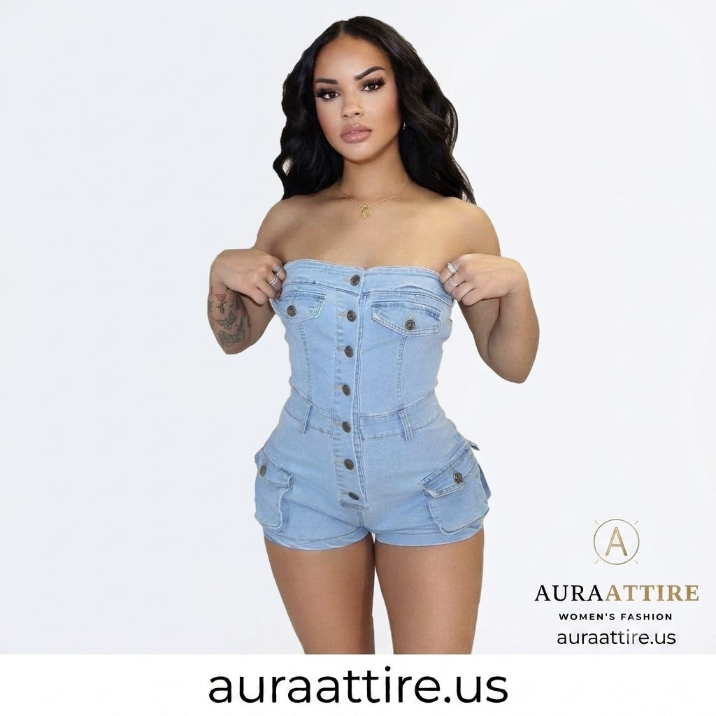 A woman modeling a light blue denim strapless romper with front buttons and flap pockets, posed against a plain white studio background. The brand name AURA ATTIRE is visible in the lower right corner.
