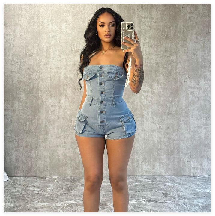 Woman taking a mirror selfie wearing a denim romper against a gray wall.