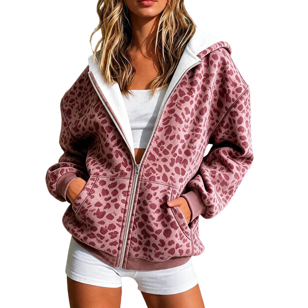 A woman wearing a pink leopard-print zip-up hoodie with a white inner lining, styled over a white crop top and white shorts against a plain white background.
